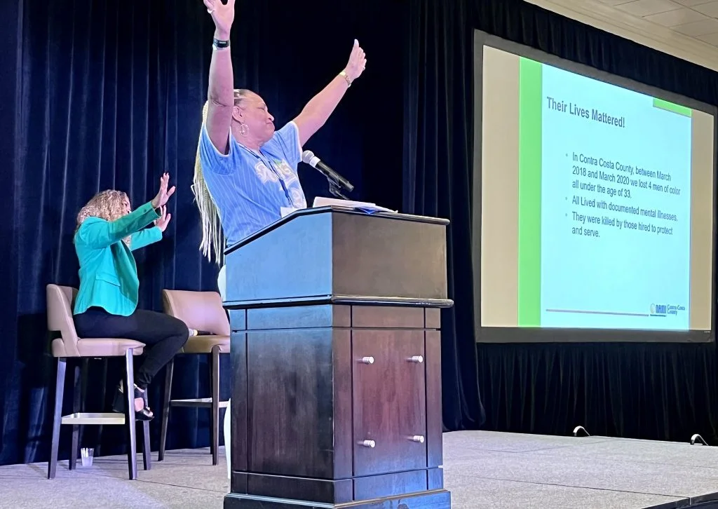 Person standing on stage with hands outstretched while giving a presentation.