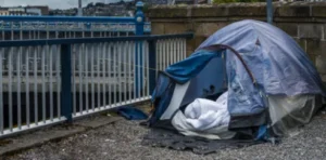 A picture of an unsheltered person's tent, outdoors in front of a fence along a wall.